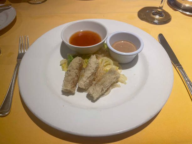 istock A white plate of three Thai Spring Rolls; deep-fried with minced shrimp, vegetables, peanuts, and sweet chili sauce. Silverware surrounds the dish, along with glass of water. 2188736361