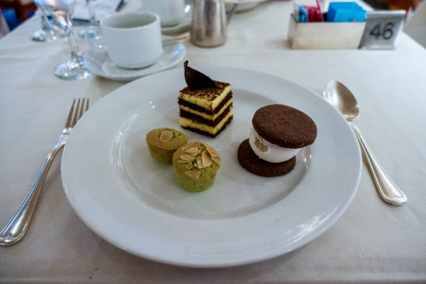 A plated dessert trio featuring layered cake with chocolate garnish, two green almond-topped pastries, and an ice cream sandwich with chocolate cookies, elegantly served on a white plate. A plated dessert trio featuring layered cake with chocolate garnish, two green almond-topped pastries, and an ice cream sandwich with chocolate cookies, elegantly served on a white plate. plated chocolate dessert stock pictures, royalty-free photos & images