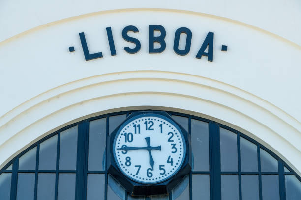 Close-up of a round Roman clock with Lisboa text above, surrounded by modern windows and a white facade with minimalist details.