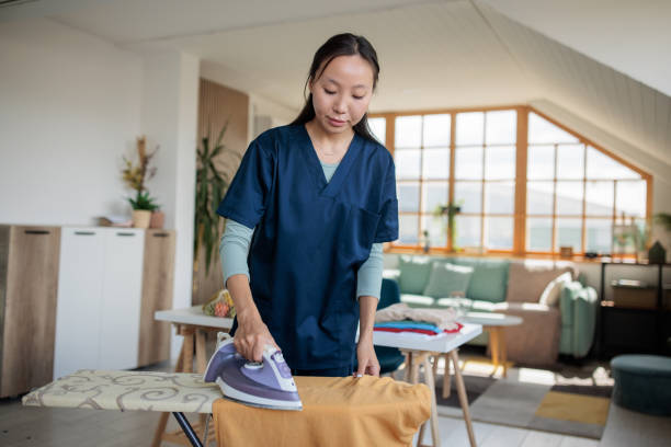 Kazakh woman nurse in medical scrubs takes care of household chores, ironing clothes after returning home from work.