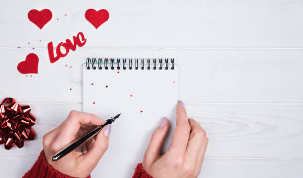 istock Woman's hands write a romantic congratulation to Valentine's Day in a notebook. Valentine's Day holiday concept. Top view. Copy space. 2188746584