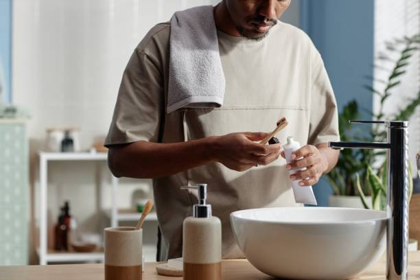 istock Black Man Holding Toothpaste Standing at Sink Preparing to Brush Teeth in Bathroom 2188762065