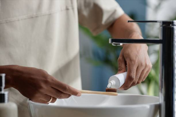 istock Hands of Black Man Holding Bamboo Toothbrush Applying Toothpaste in Bathroom 2188762075