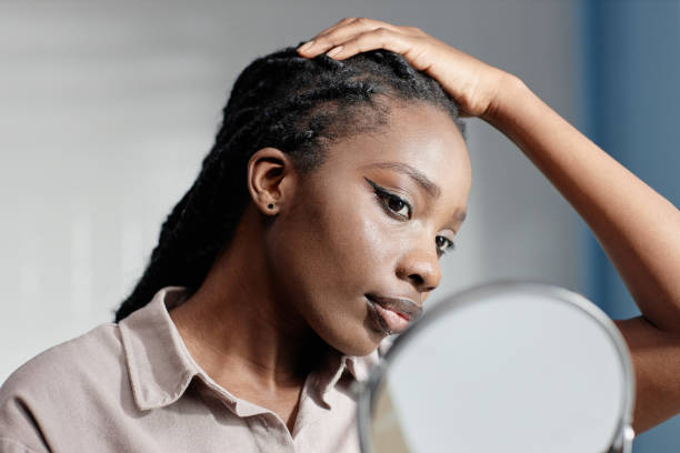 Black Woman Touching Hair Looking in Mirror during Self Care Routine in Bathroom