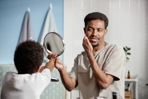 istock Smiling Man Looking in Mirror while Son Helping Dad while Cleaning Skin in Bathroom 2188762105