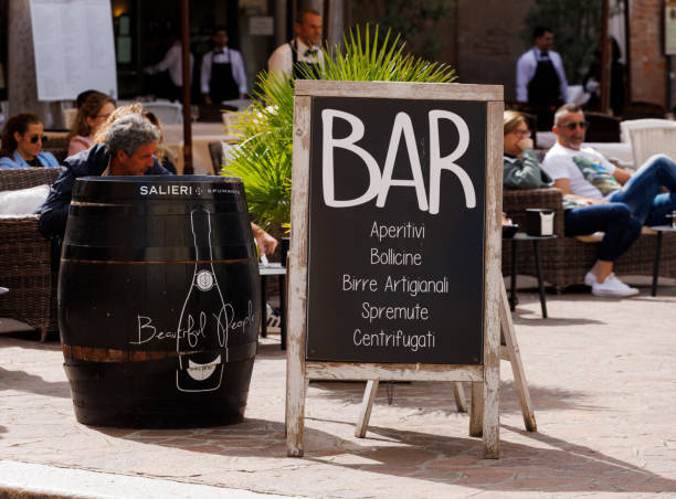 Mantova, Italy - September 15, 2024: A corner of an Italian square featuring a black barrel and a chalkboard advertising a bar with its offerings, including aperitifs and freshly squeezed juices