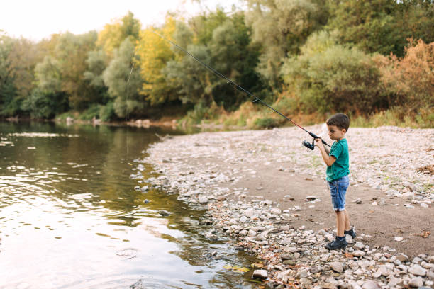 A boy is fishing alone from the shore.