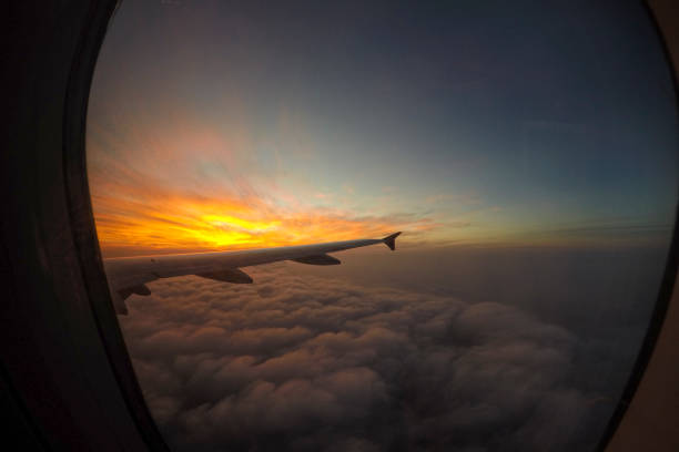 As the airplane soars above the clouds, a vibrant sunset paints the sky in stunning hues of orange and purple, creating a breathtaking view for travelers en route to Cambodia.