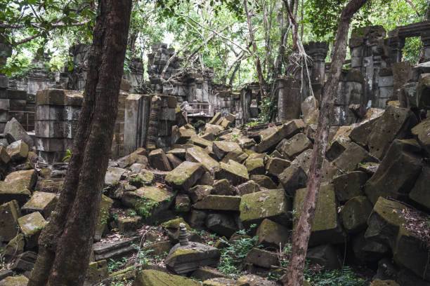 Ancient blocks of stone lie scattered in the remnants of Angkor Wat, surrounded by lush greenery. The temple ruins reflect the passage of time in this historical site in South East Asia.