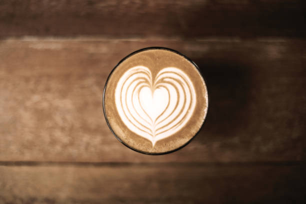 Heart-shaped latte art on coffee table viewed from above A beautifully crafted latte with heart-shaped foam art, set against a wooden table. Perfect for coffee enthusiasts and baristas. Demonstrating color of 2025 year. food sample cups stock pictures, royalty-free photos & images