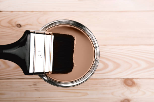 Paintbrush dipped in brown paint on light wooden background showing texture