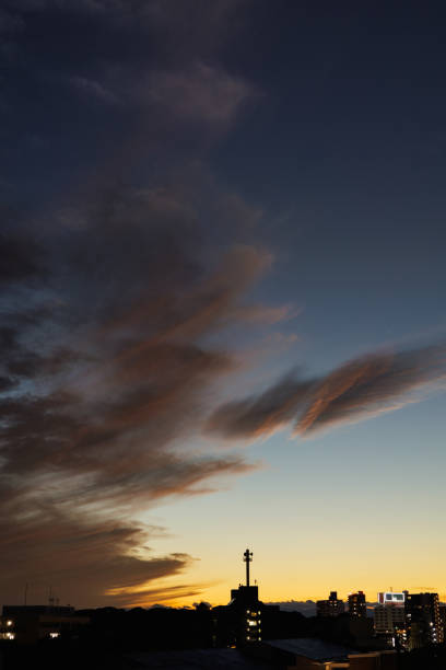 Light streaks of orange string across vertically stacked wispy clouds floating in the dusk sky, creating the appearance of dimly glowing embers in a campfire.