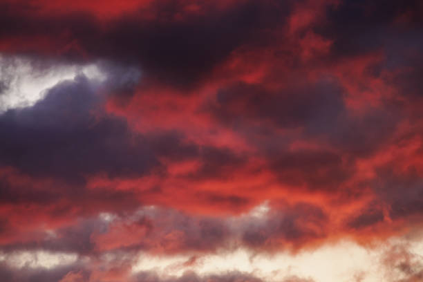 Appearances can be deceiving as a tranquil morning sky becomes illuminated by the approaching sunrise’s fiery hues of blood red and vibrant orange, creating a dramatic cloudscape.