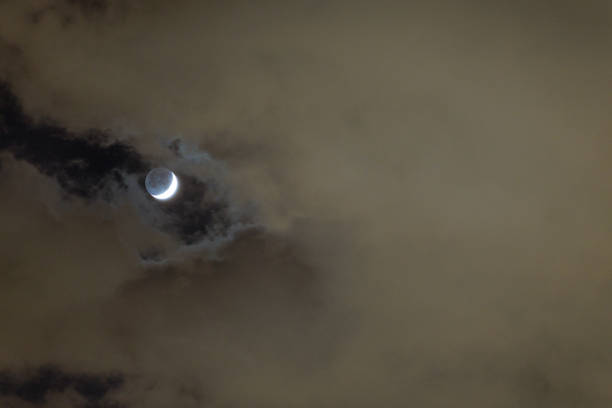 A waxing crescent moon appears through a break in the clouds, showing its earthshine along with a brilliant crescent.