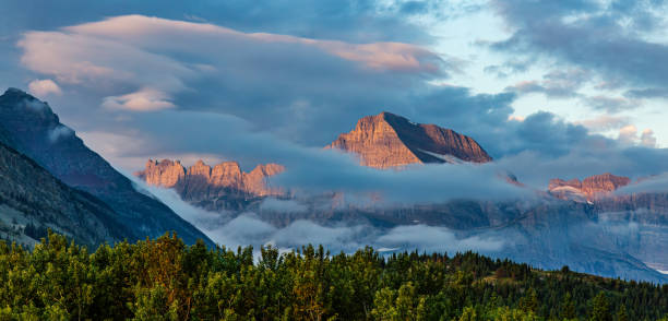 A breathtaking view of a majestic mountain peak surrounded by lush greenery and dramatic clouds during sunset, capturing the beauty and serenity of nature.