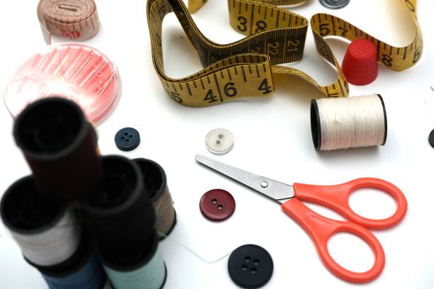 Flat lay of sewing tools featuring thread spools, a flexible measuring tape, scissors, buttons, and a thimble