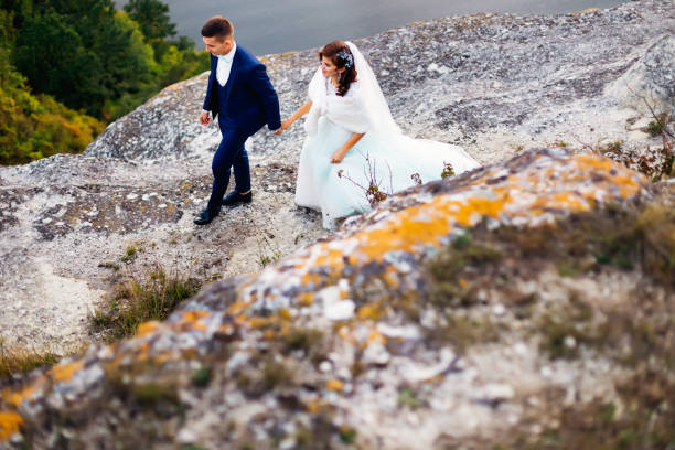rocky river bank. newlyweds hold hands and walk. top-down view