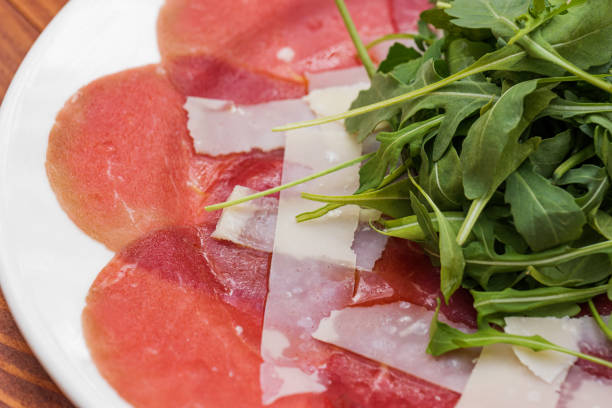 Red beef carpaccio in a white plate with arugula and parmesan cheese