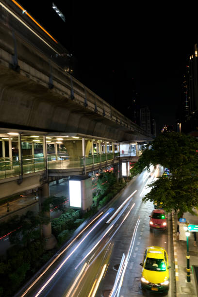Vehicles light trails under Bts skytrain track on Sukhumvit road by night, Bangkok, Thailand.