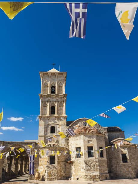 Iconic stone church with a bell tower and decorative flags, showcasing historical architecture in Larnaca, Cyprus.