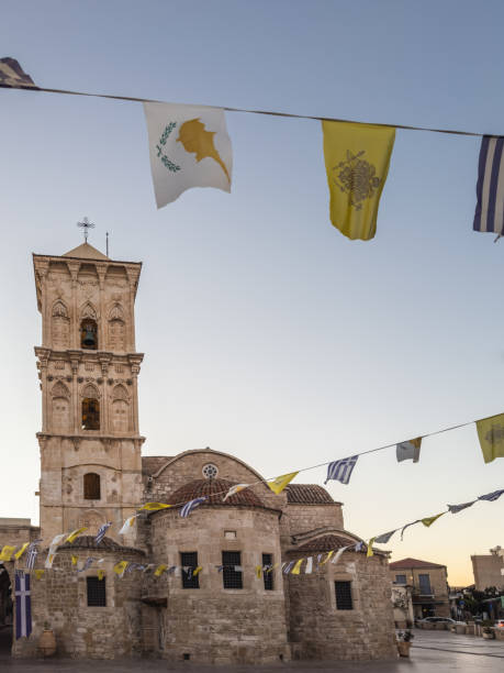 Iconic stone church with a bell tower and decorative flags, showcasing historical architecture in Larnaca, Cyprus.