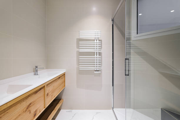 istock Modern bathroom with wooden base for white sinks. Radiator for warm water procedures in winter. Shower zone with glass door. Bathroom decorated with light tiles. 2188848331