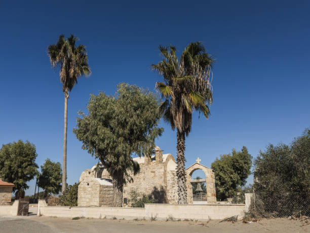 The ruins of Saint George Church, with palm trees and a bell tower, set against the clear blue sky, evoking a sense of history and serenity in Cyprus.