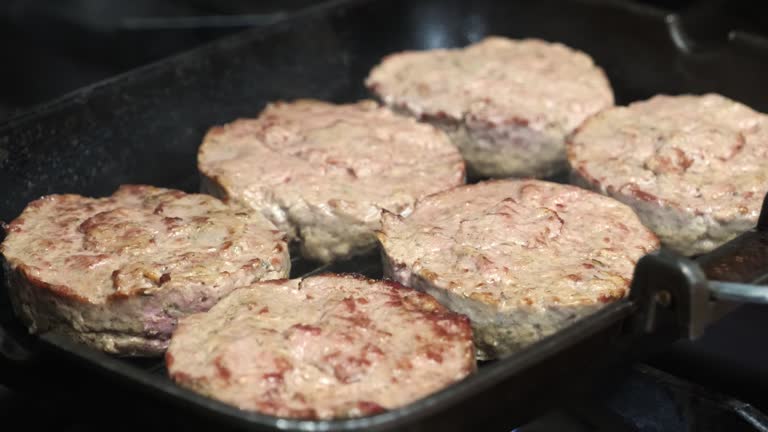 Meat burgers frying on hot grill pan in fastfood restaurant. Close-up of pork cutlets cooking for hamburgers.