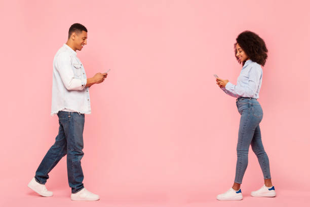 istock Black man and woman using cellphones and texting, walking on pink studio background, full length shot. New mobile application advertisement 2188866272