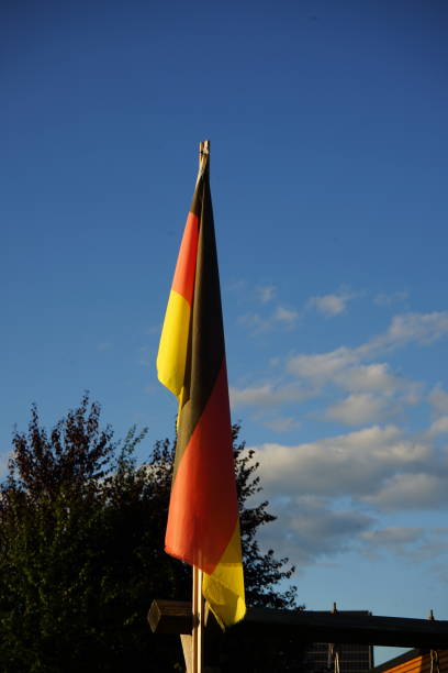 The German flag waving in the wind, featuring clear stripes of black, red, and gold against a blue sky. A symbol of pride and identity.