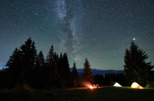 istock Amidst forested mountain landscape, two tents glow warmly beside campfire under star-filled sky. 2188869524