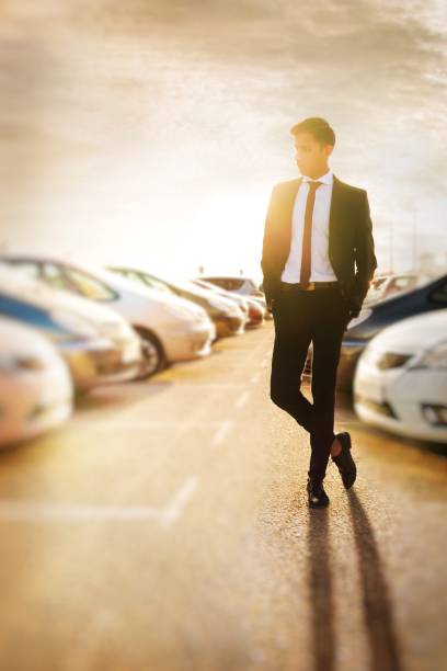 A tall your man in black suit standing at the car parking lot and watching cars