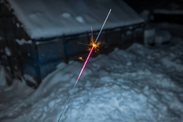 Burning sparkler glowing brightly outdoors on snowy winter night.