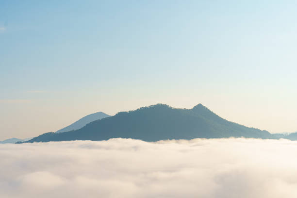 A serene landscape featuring mountains emerging from sea of clouds under clear blue sky, evoking sense of tranquility and peace