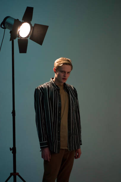 istock Young blond man in striped shirt standing in studio in dim light 2188878786