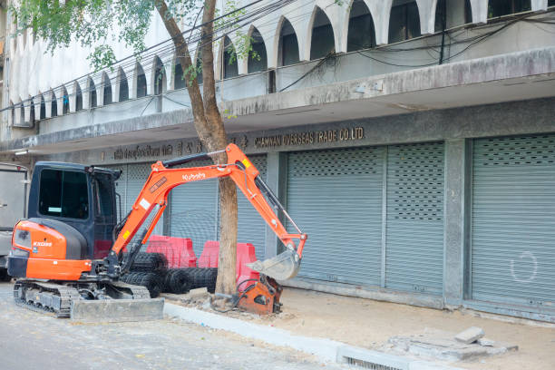 Digger in street with sidewalk construction in Bangkok Pom Prap Sattru Phai. Scene is in street Damrong Rak Road. Sidewalk is under restoration and construction. Jalousies of stores and offices in buildings are closed. Above jalousies are letters Chamnan over Sea Trade Ltd., Part.