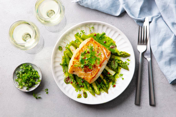 Roasted cod, codfish with asparagus and on plate and white wine. Grey background. Close up. Roasted cod, codfish with asparagus and on plate and white wine. Grey background. Close up. cod stock pictures, royalty-free photos & images
