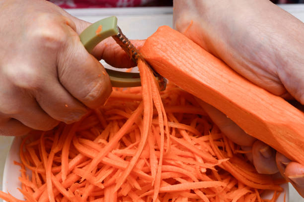 Close-up of fresh carrots being cut into thin strips with a vegetable peeler. Home cooking.