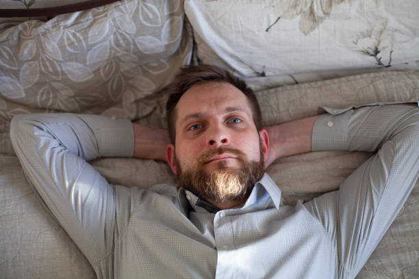 Man relaxes on a sofa at home, eyes closed, lost in peaceful thoughts. Enjoying tranquility, he finds contentment in his cozy space, taking a break from busy life