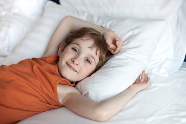 istock Pleased boy lying and smiling on a white pillows in bed. 2188893249