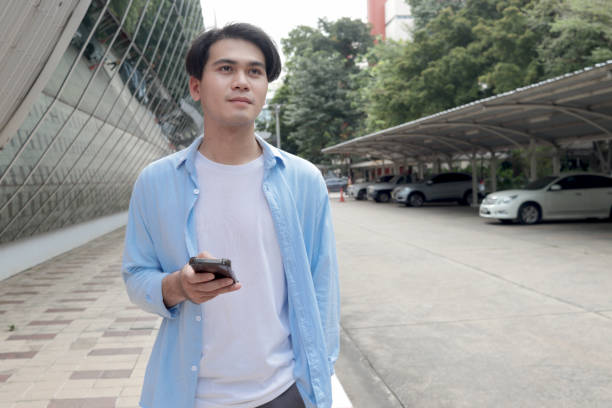 istock Asian young man casual clothes looks at mobile phone and texts message while standing in front of modern building. Male using smartphone in outdoor. Happy smart young man using electronic devices outdoors in urban modern environments. 2188899809