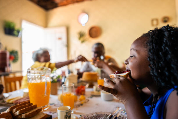 Girl eating bread with jam while having breakfast with her family at home