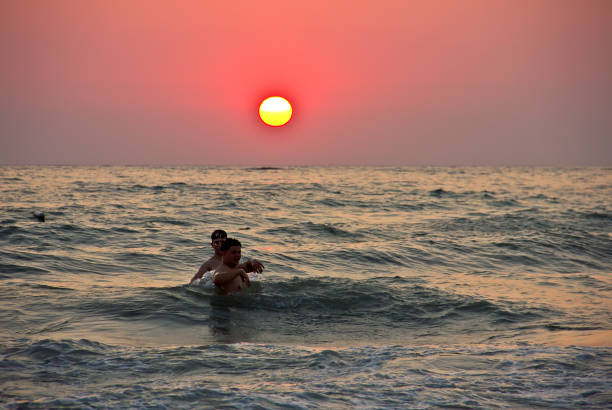 Father lifts girl with one hand on the beach in summer evening by sea at sunset. Happy family funny play airplane outdoors. Travel, vacation, holiday, tourism