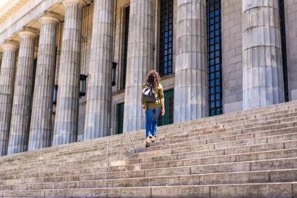 Mid distance view of three young woman meeting and hugging in Neo-Classical university building colonnade.