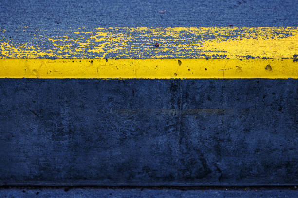 istock Closeup of a concrete surface featuring a striking yellow stripe on a dark gray asphalt background, ideal for urban, modern, and minimalistic photography themes.  Copy space 2188917424