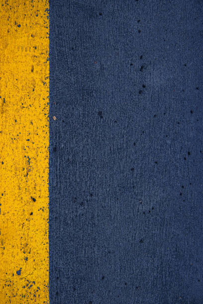 istock Closeup of a concrete surface featuring a striking yellow stripe on a dark gray asphalt background, ideal for urban, modern, and minimalistic photography themes.  Copy space 2188917435