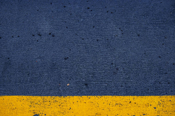 istock Closeup of a concrete surface featuring a striking yellow stripe on a dark gray asphalt background, ideal for urban, modern, and minimalistic photography themes.  Copy space 2188917500