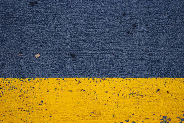 istock Closeup of a concrete surface featuring a striking yellow stripe on a dark gray asphalt background, ideal for urban, modern, and minimalistic photography themes.  Copy space 2188917504