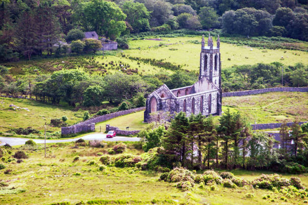 A small church sits in a field with a fence around it. The church is old and has a stone tower. The grass is green and the sky is cloudy