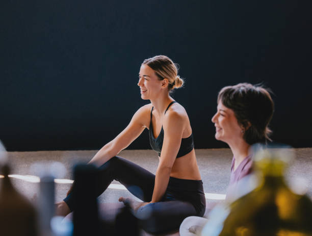 Two women enjoy a peaceful yoga session in a sunlit studio, promoting wellness and positivity. Their smiles reflect relaxation and mindfulness in a serene environment.
